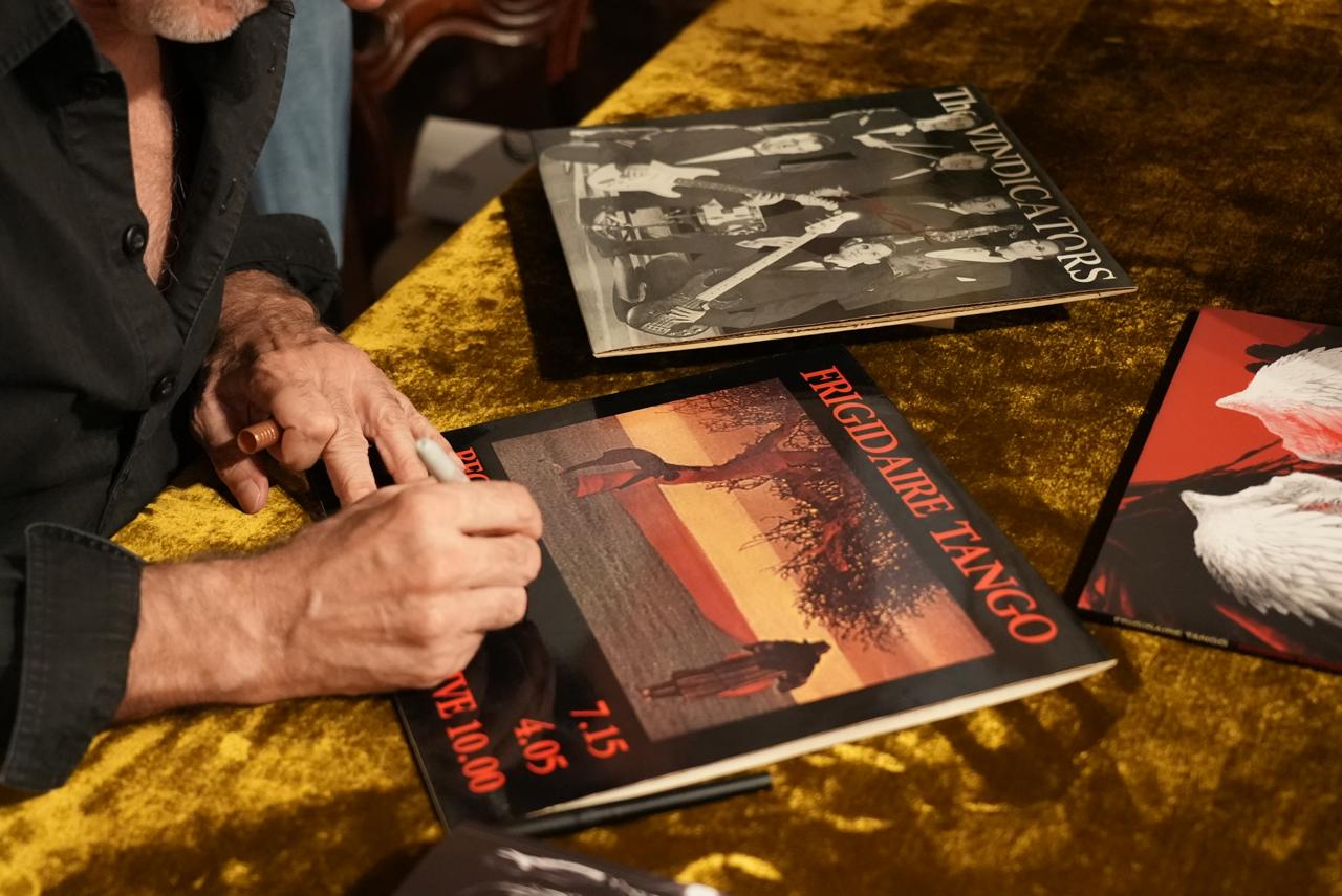 Una mano firma la copertina di un disco dei Frigidaire Tango, accanto a un secondo LP